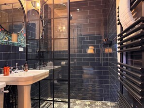 A bathroom with a glass shower enclosure, a white sink, and black tiled walls.