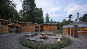 A circular wooden building with a stone patio, outdoor seating, and a central fire pit.