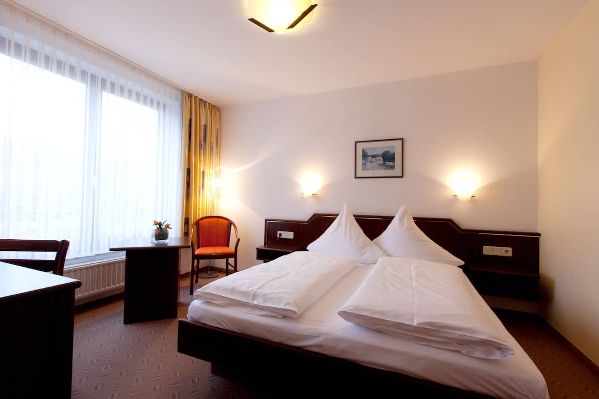 Une chambre d’hôtel avec un lit bien fait, une chaise, une table et une fenêtre avec des rideaux.
