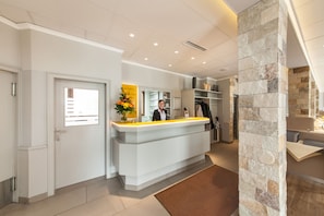 A reception area with a white reception desk, a potted plant, and a stone pillar. - Hotel Strijewski (Wolfsburg)