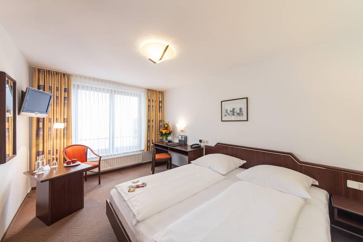 Une chambre d’hôtel équipée d’un lit, d’un bureau, d’une chaise, d’une télévision et d’une fenêtre avec des rideaux.