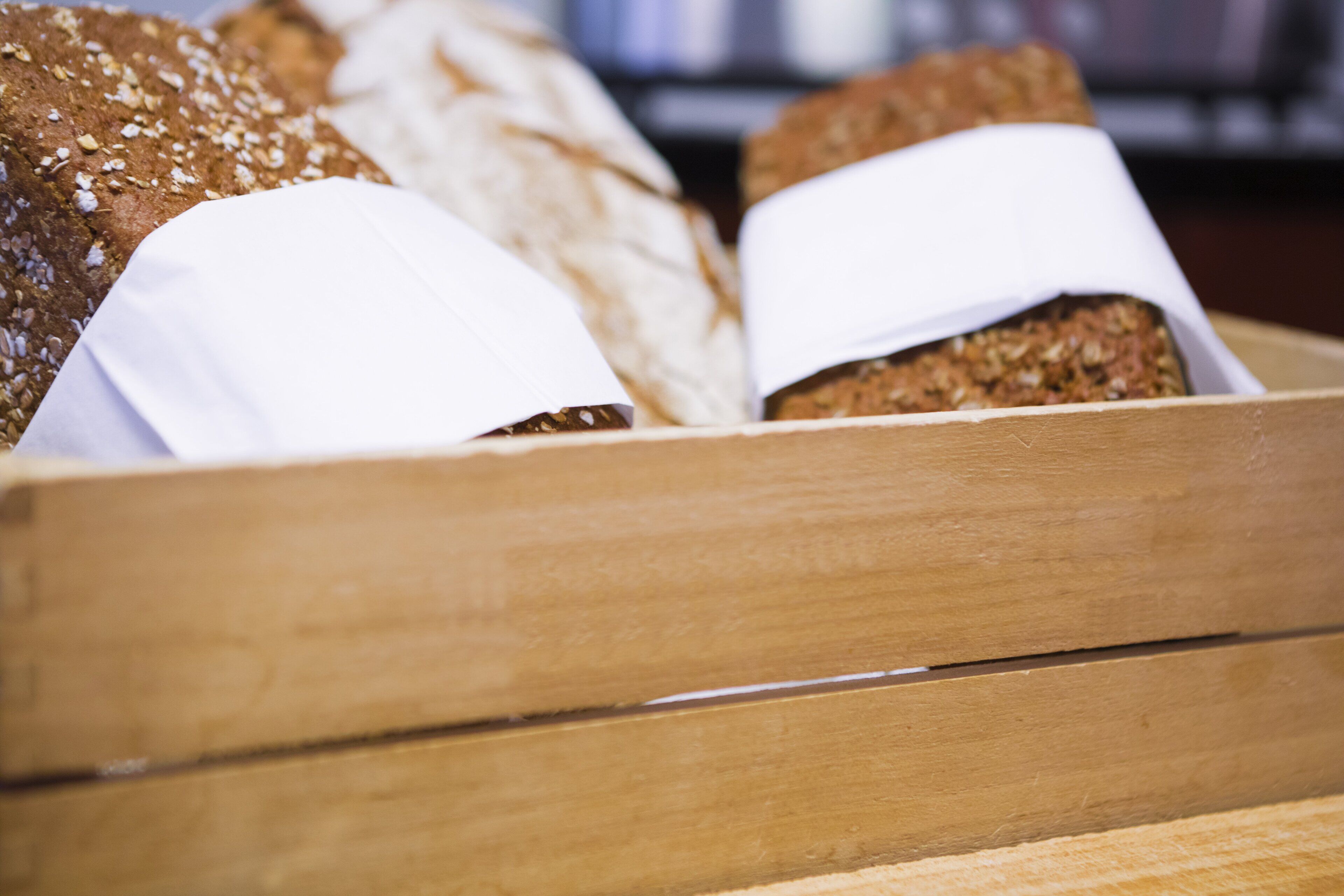Una caja de madera con diferentes tipos de pan, algunos envueltos en papel blanco.