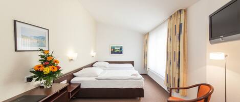 A hotel room with a bed, a desk, a chair, a TV, and a window with curtains.