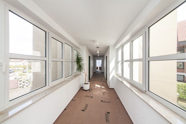 A corridor with large windows on both sides, a potted plant, and a visible outdoor area with parked cars and greenery. - Hotel Strijewski (Wolfsburg)
