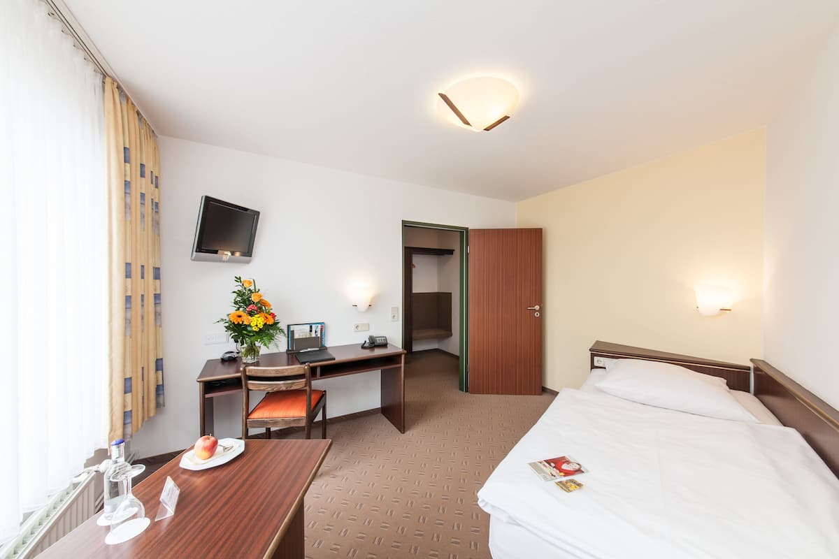 Une chambre d’hôtel comprenant un lit, un bureau avec une chaise, un téléviseur fixé au mur et une porte donnant sur une autre pièce.