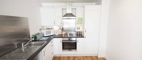 A compact kitchen with white cabinets, a stainless steel range, a microwave, and a dishwasher.
