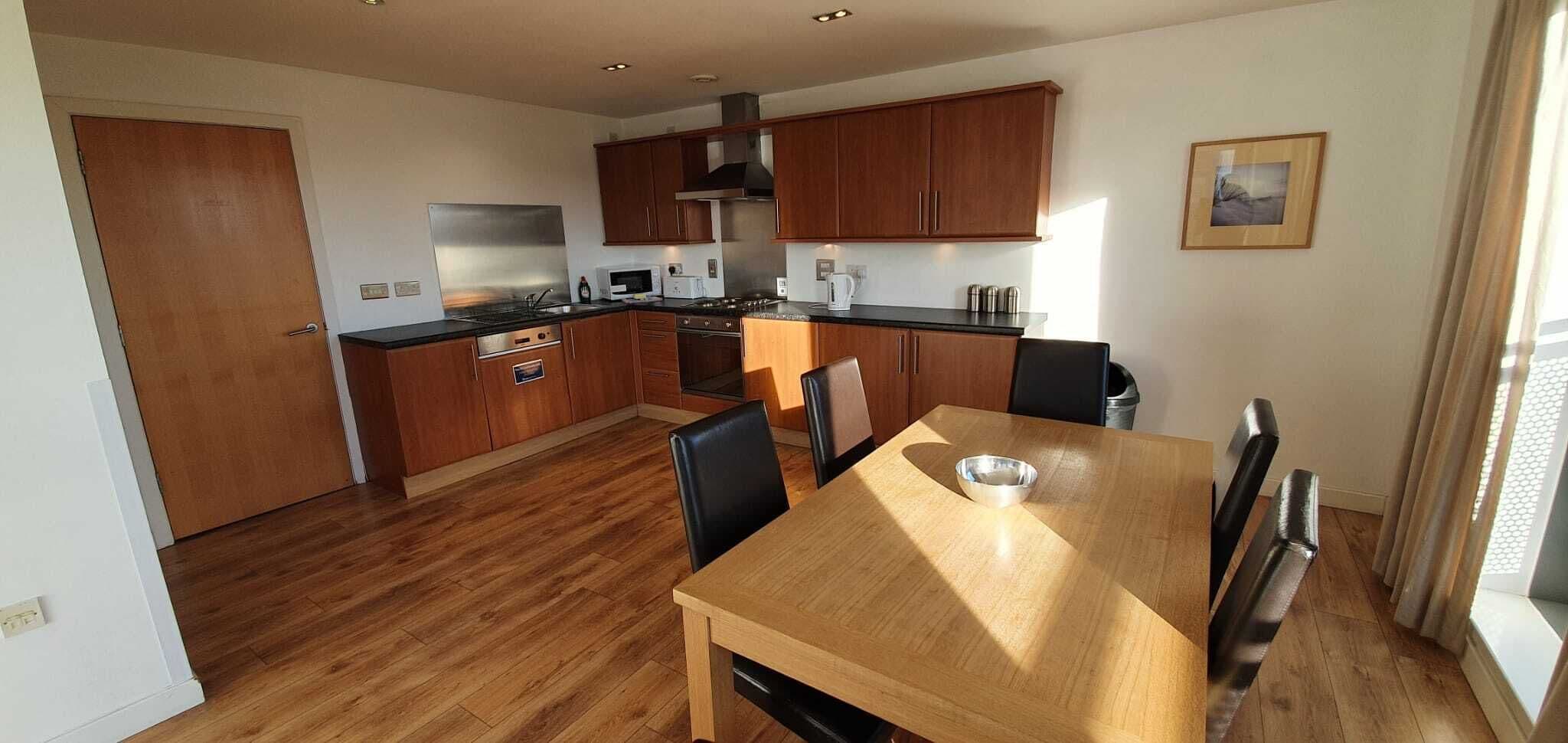 A modern kitchen with wooden cabinets, a stainless steel range hood, and a dining area with a wooden table and chairs.