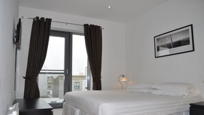 A bedroom with a bed, a desk, a lamp, and a window with curtains. - Ocean Serviced Apartments (Edinburgh)