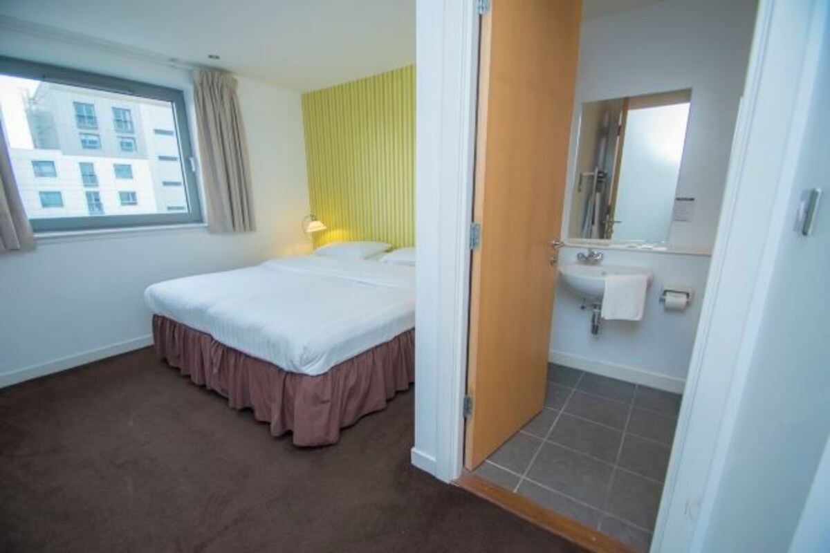 A hotel room with a bed, a window, a bathroom with a sink and mirror.