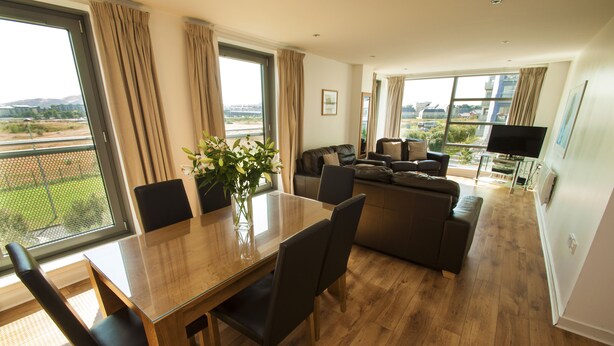 A spacious living area with a dining table, chairs, a sofa, and a TV. - Ocean Serviced Apartments (Edinburgh)