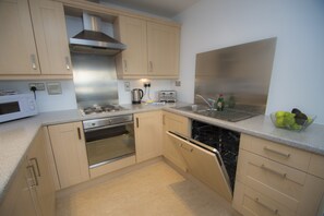A modern kitchen with beige cabinetry, stainless steel appliances, a dishwasher, and a countertop with a fruit bowl. - Ocean Serviced Apartments (Edinburgh)