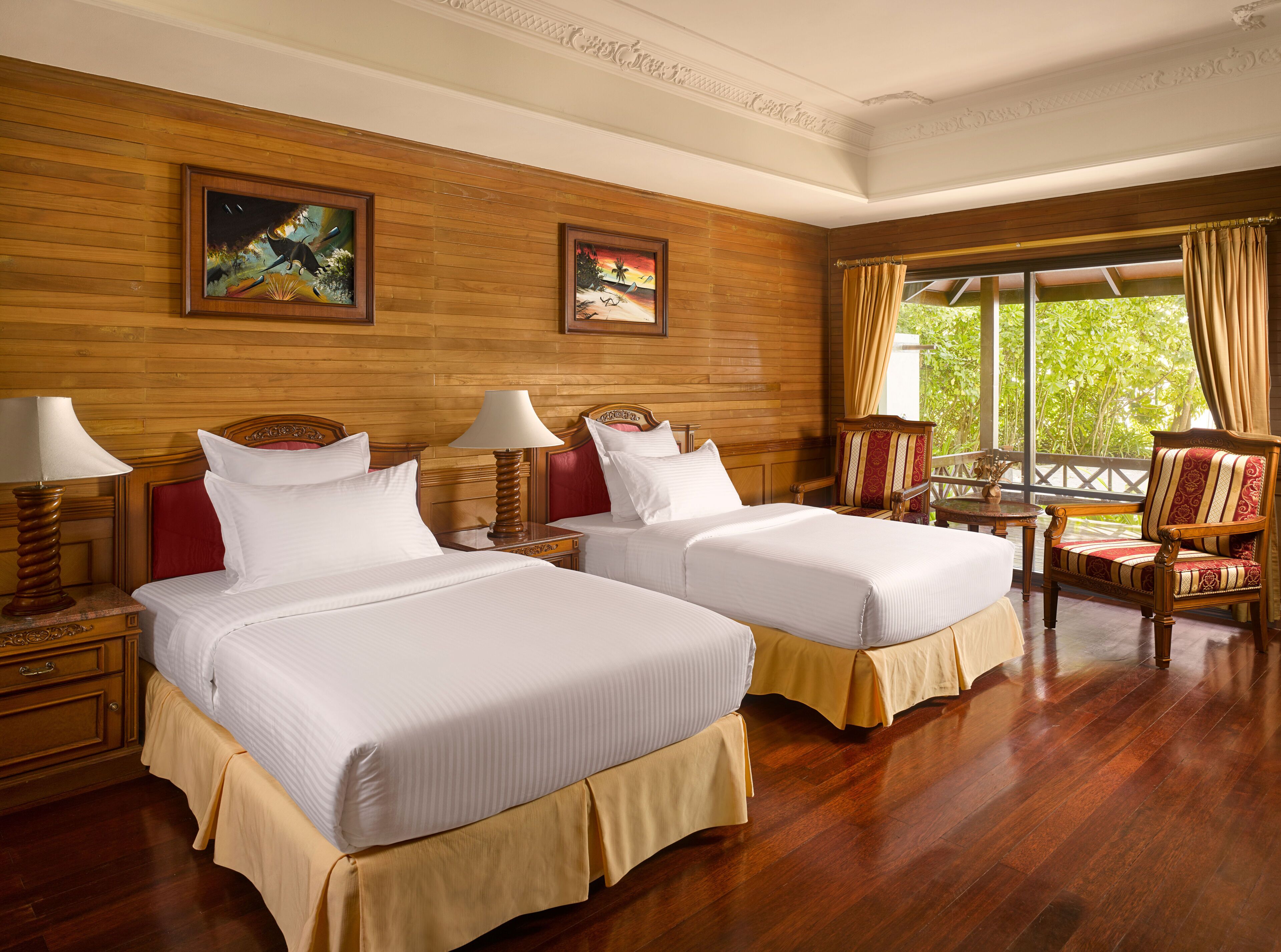 A hotel room with two beds, wooden paneling, a balcony with a view, and artwork on the walls.