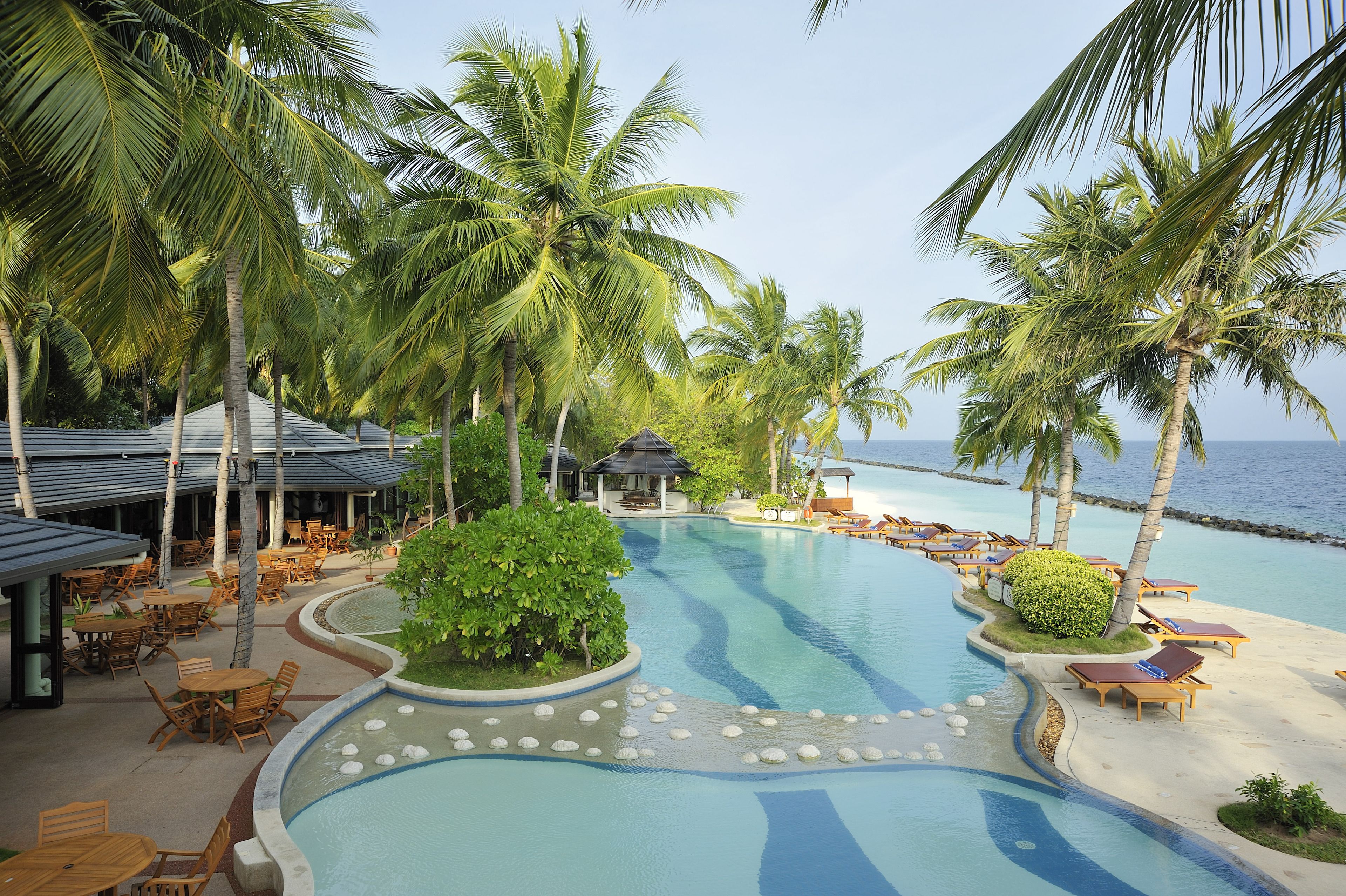 A resort pool area with palm trees, lounge chairs, and a small gazebo.