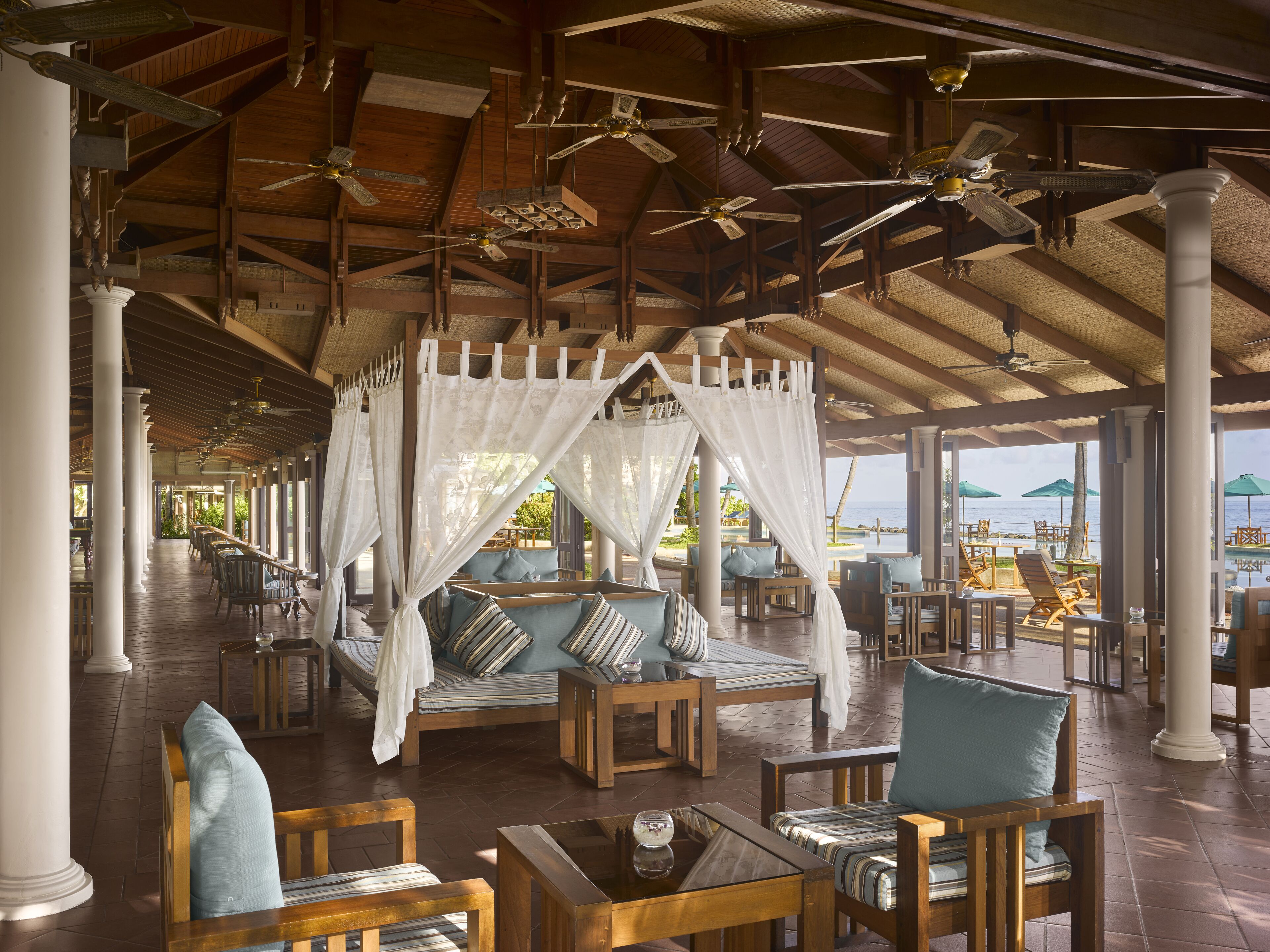 A spacious lounge area with wooden furniture, a canopy bed, and ceiling fans.