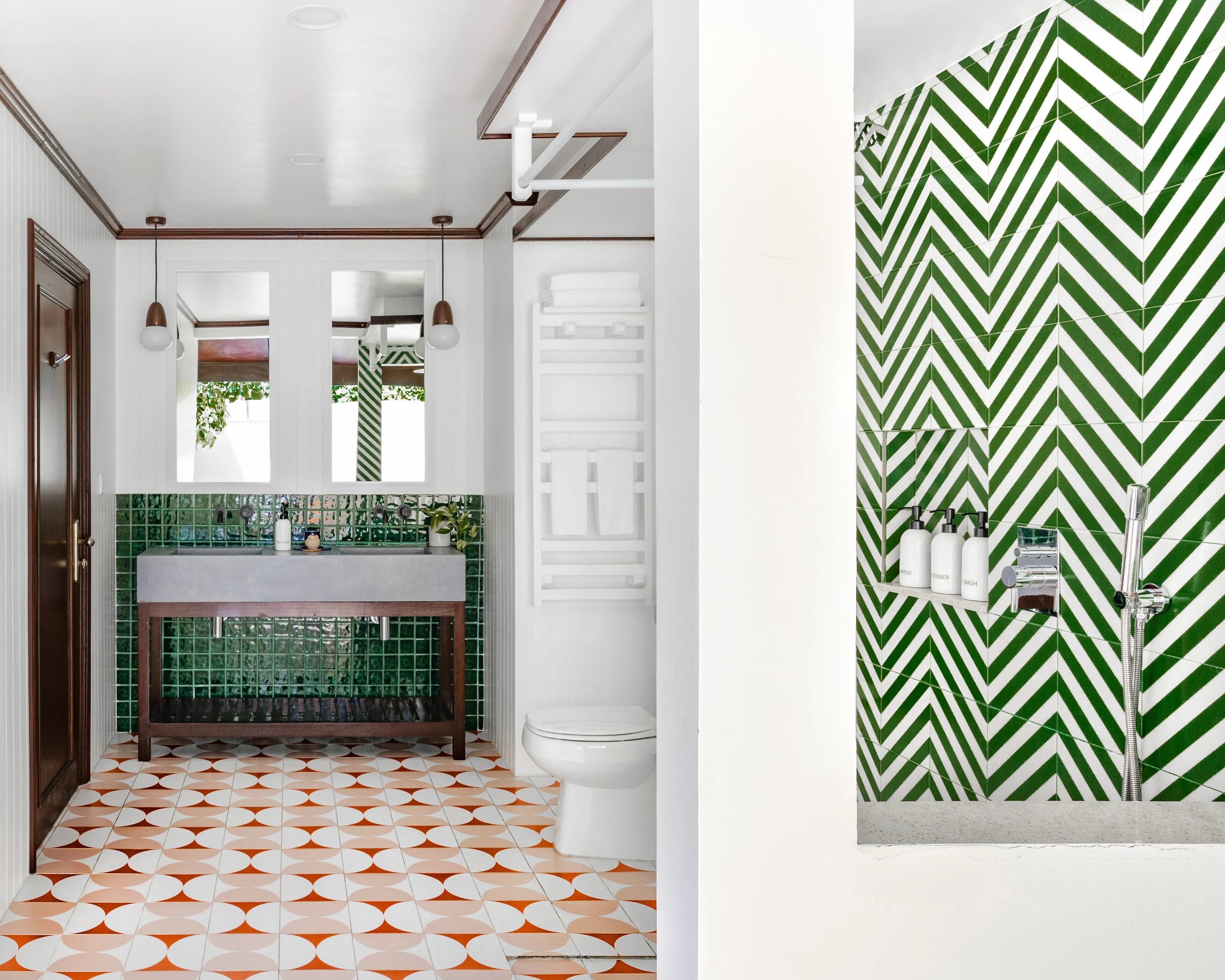 Een badkamer met een groen betegeld wastafelblad, een wit toilet en een douchewand met een zigzaagpatroon.