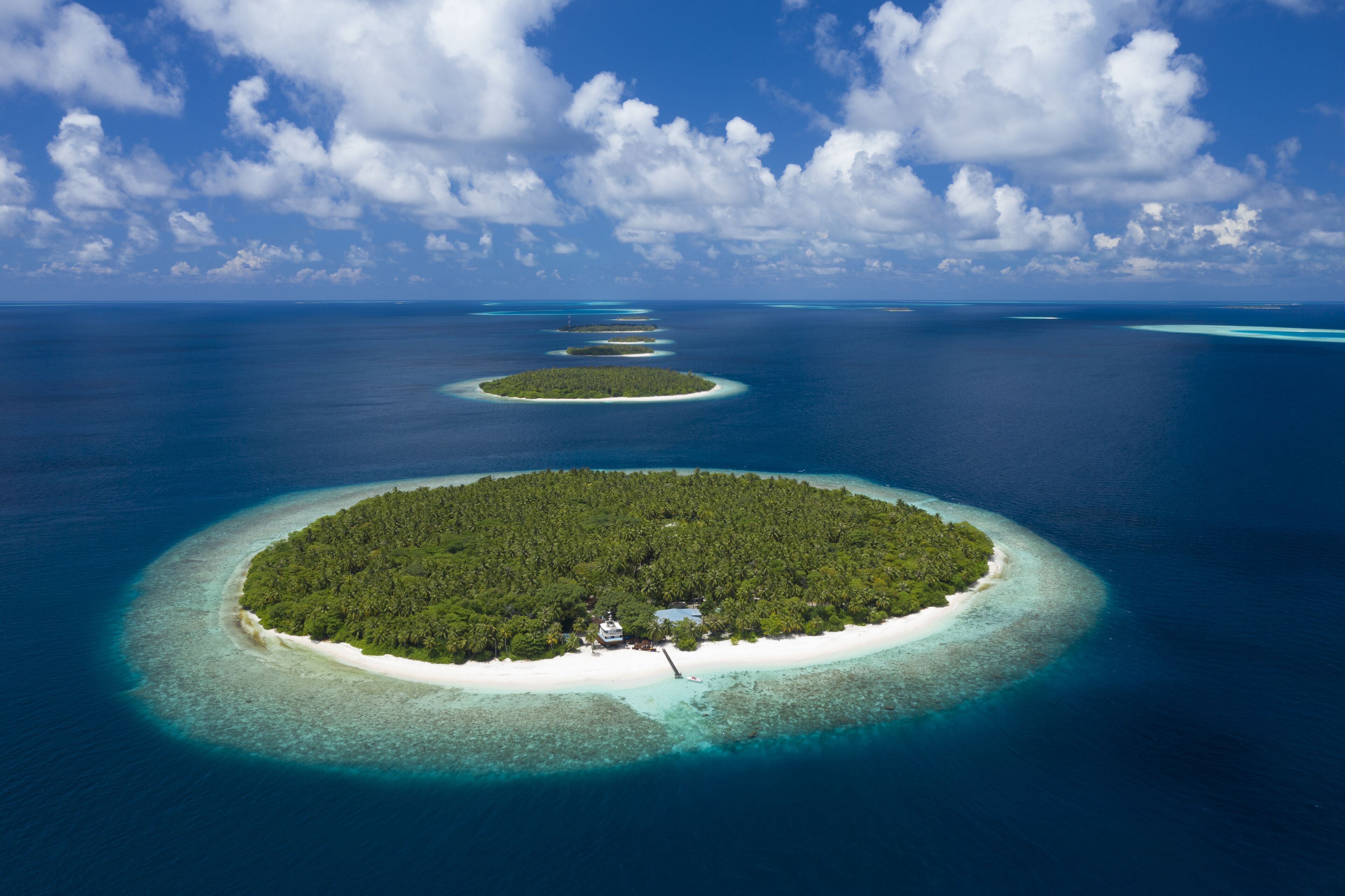 An aerial view of a tropical island with a central building surrounded by lush greenery and clear blue waters.