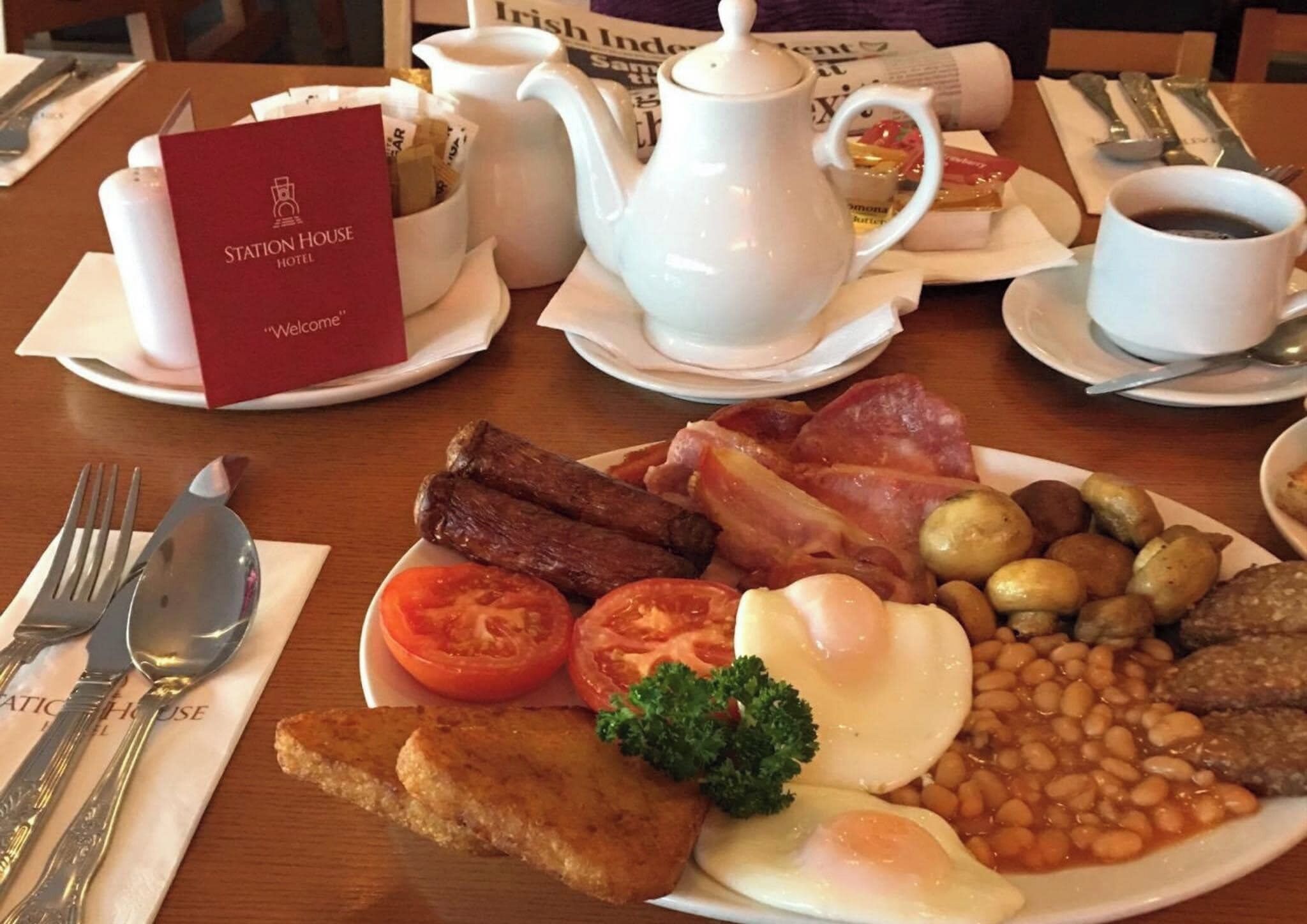 A breakfast setting with a plate of eggs, bacon, sausages, tomatoes, beans, and toast.