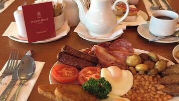 A breakfast setting with a plate of eggs, bacon, sausages, tomatoes, beans, and toast.
