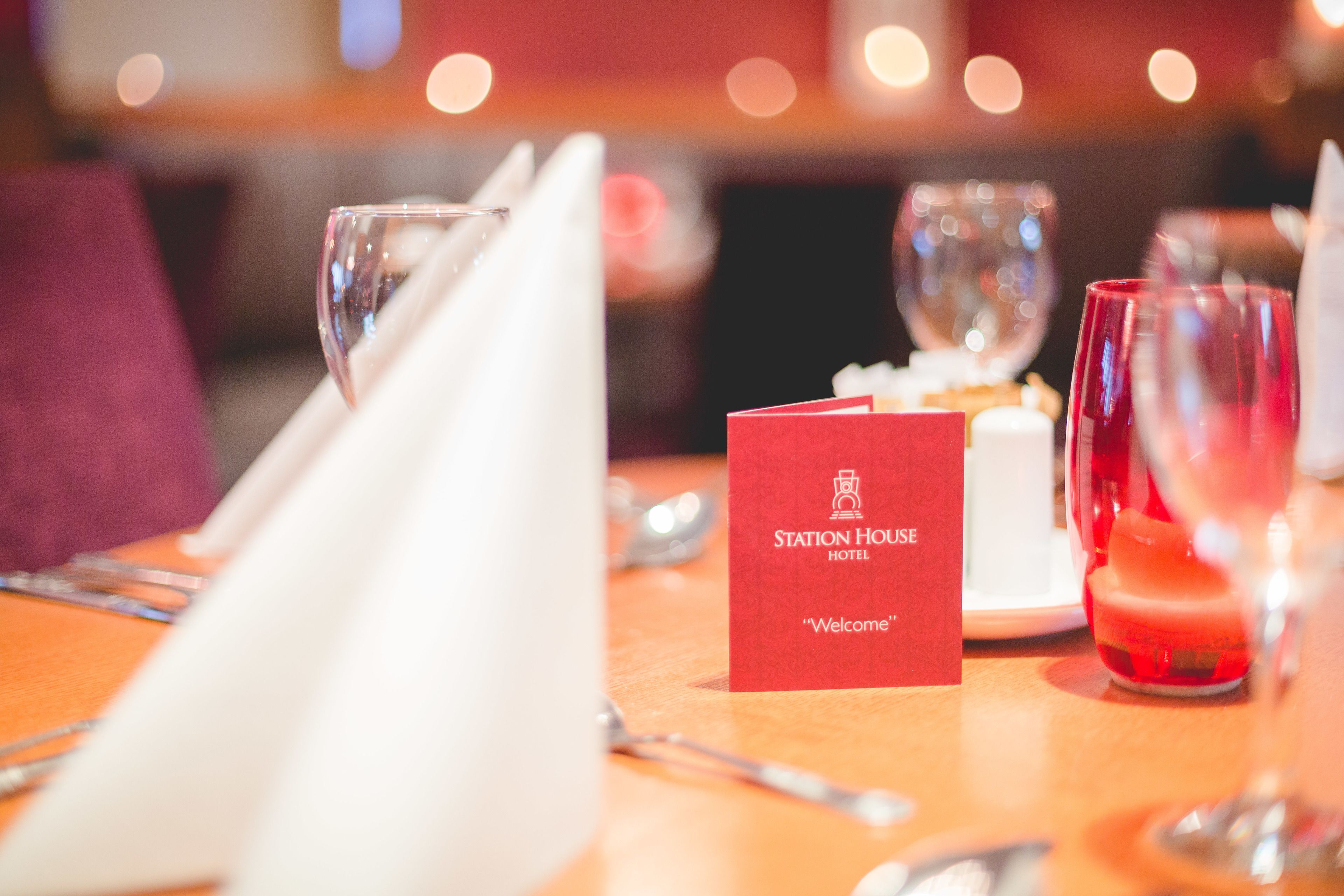 A dining table set with a red welcome card, glasses, and a candle.