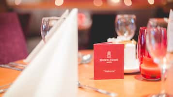 A dining table set with a red welcome card, glasses, and a candle.