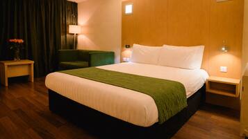 A hotel room with a large bed, a green chair, a nightstand, and a lamp.
