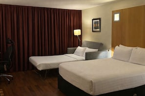 Habitación de hotel con dos camas individuales, un escritorio, una silla, una lámpara y un cuadro en la pared.
