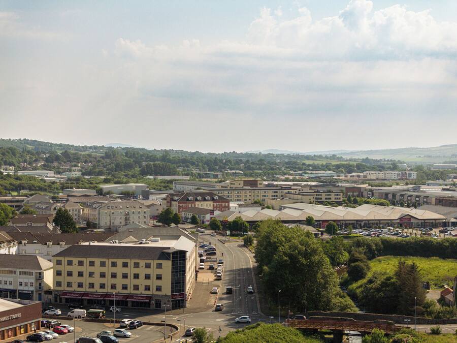 A town with a mix of commercial and residential buildings, a main road with cars, and a bridge in the foreground.