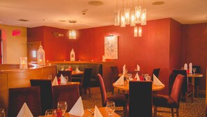 A restaurant with red walls, multiple tables with white napkins, and hanging light fixtures. - Station House Hotel (Letterkenny)