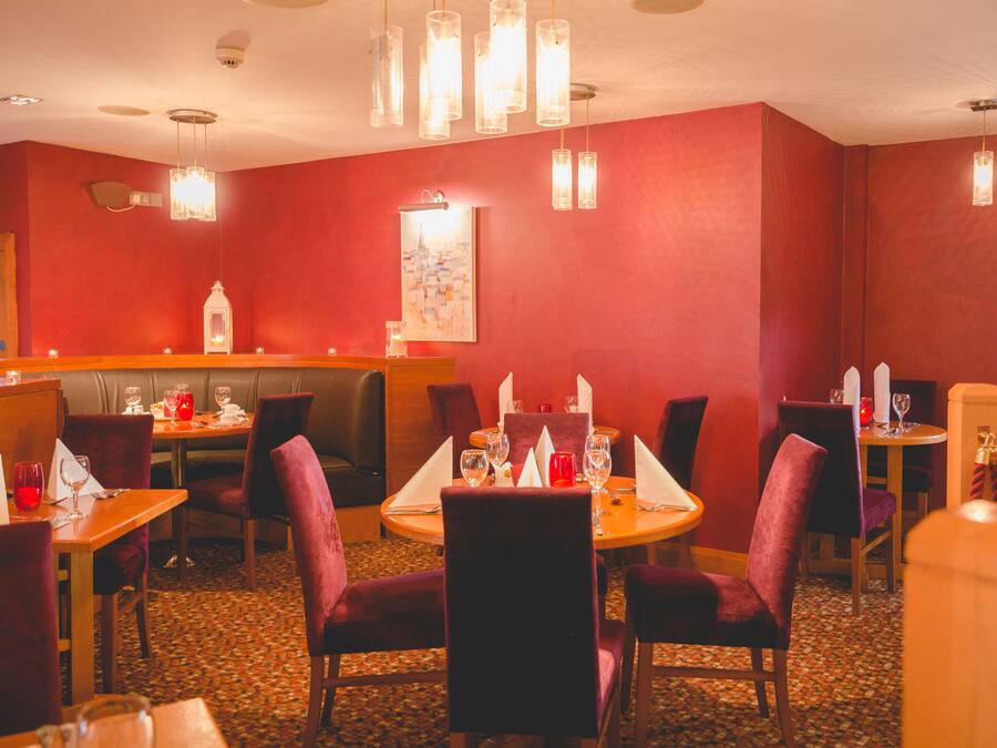 A restaurant with red walls, round tables, and purple chairs.