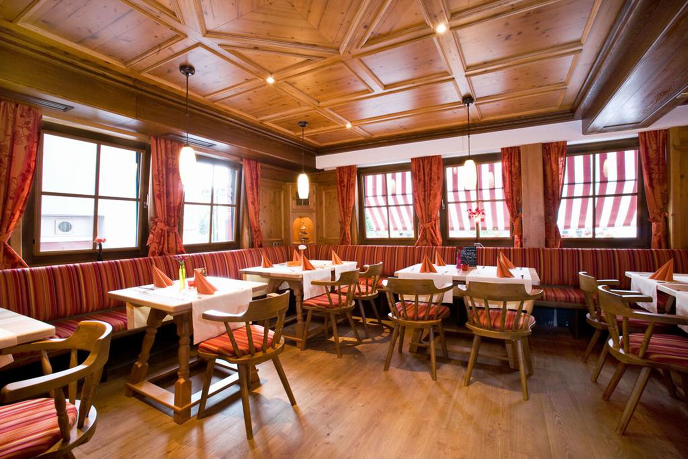 Ein Restaurant mit Holzvertäfelungen, gepolsterten Sitzbänken mit Streifenmuster und Tischen mit weißen Tischdecken.