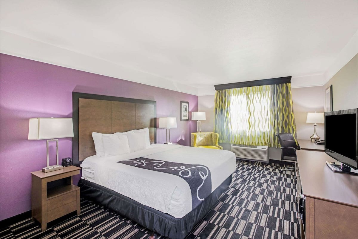 A hotel room with a bed, bedside tables, a desk with a TV, a chair, and a window with curtains.