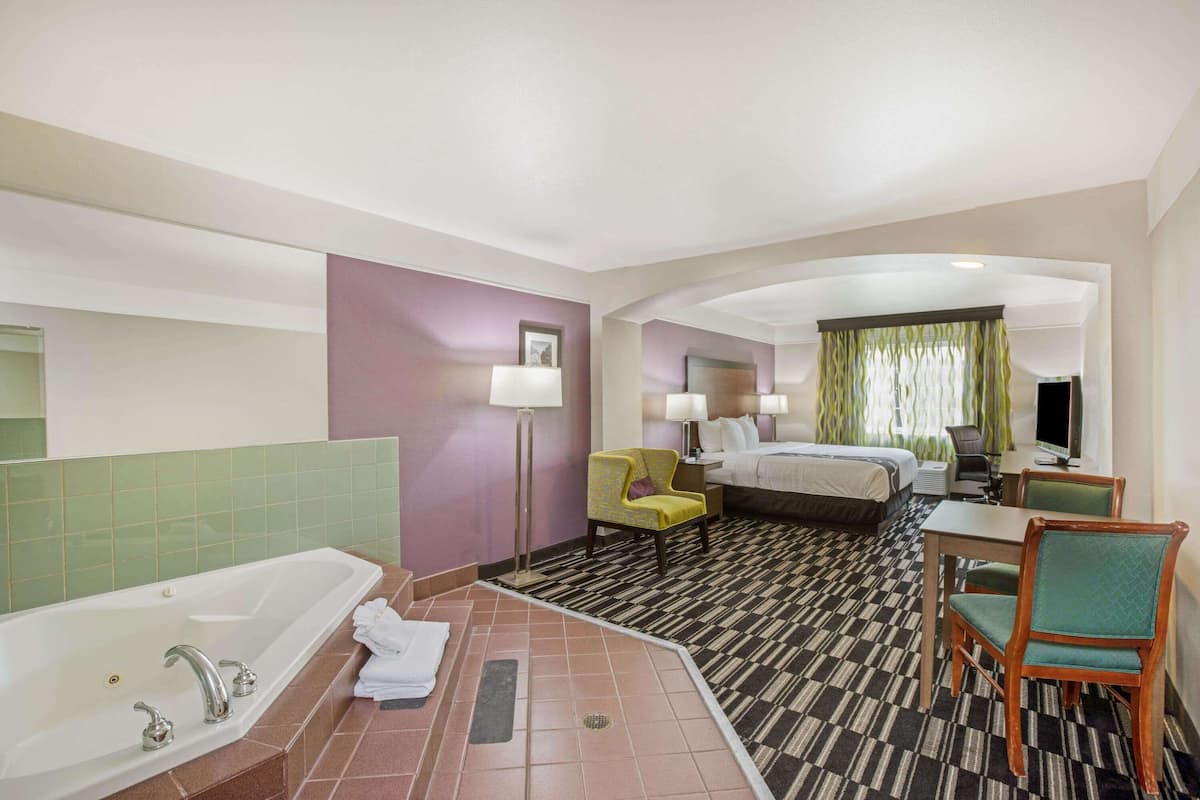 A hotel room with a large bathtub, a bed, a desk with a chair, and a small table.