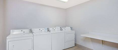 A laundry room with four stacked washers and dryers, a white shelf, and a fluorescent ceiling light.