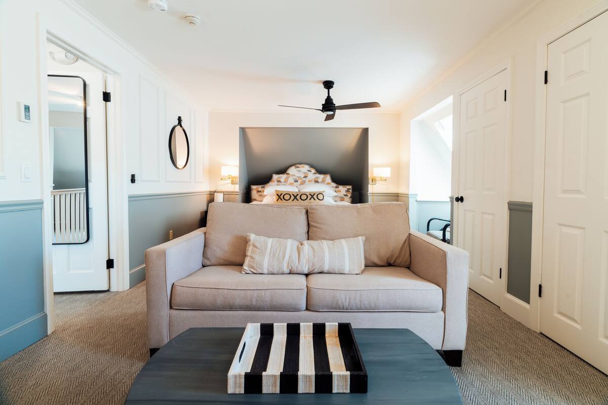 A hotel room with a beige sofa, a black and white striped tray table, a ceiling fan, and a wall-mounted mirror.