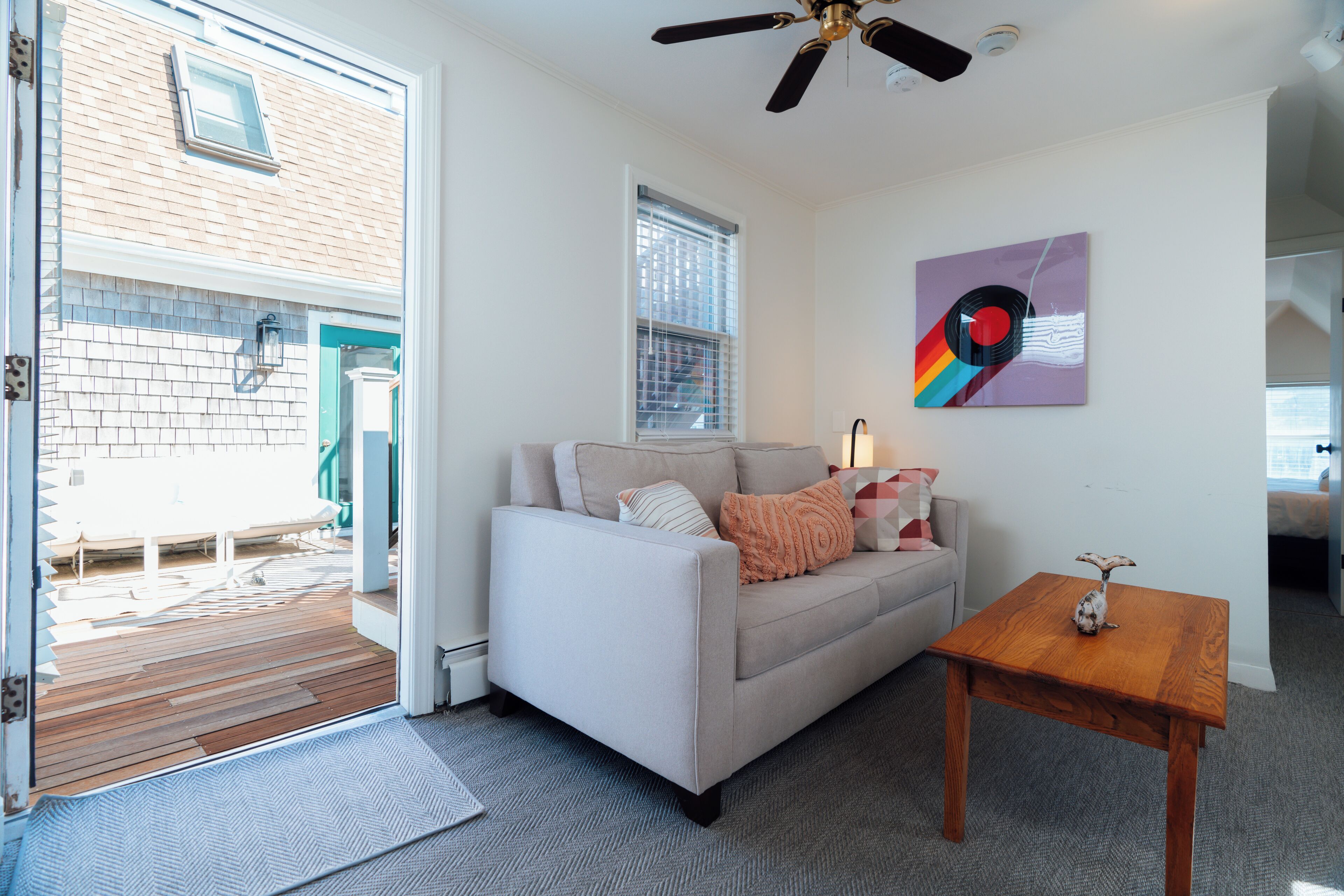A living room with a sofa, a wooden coffee table, a ceiling fan, and a window with blinds.