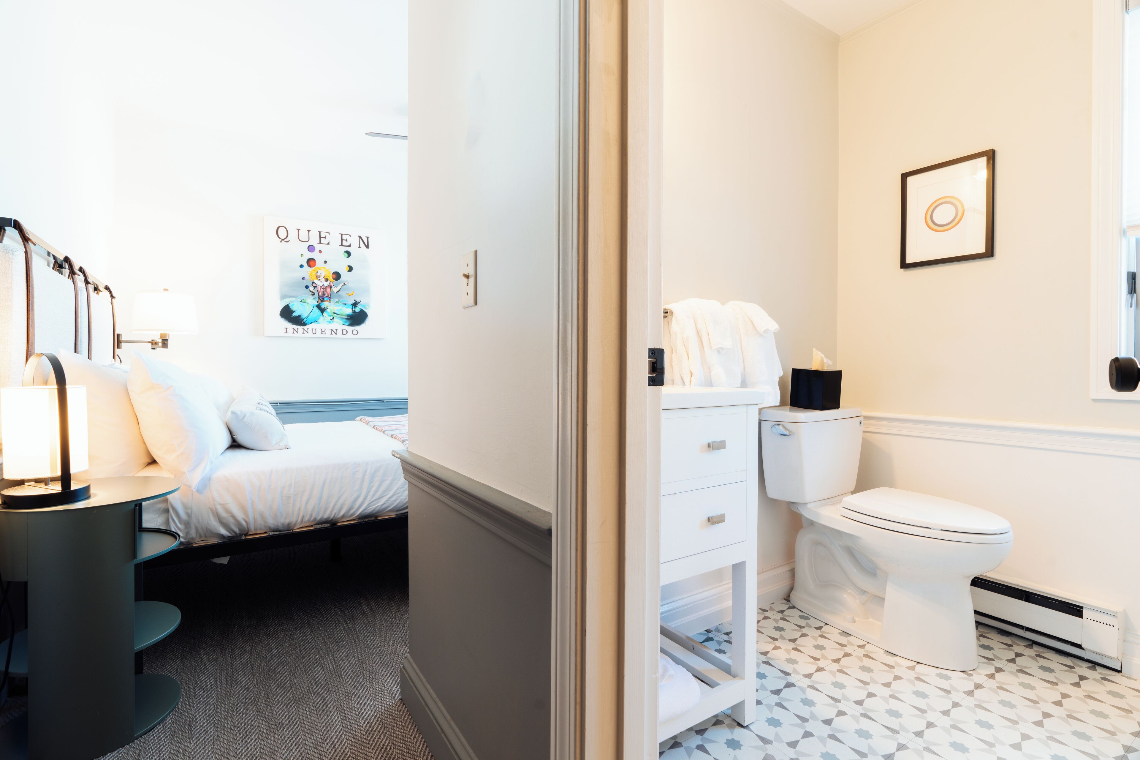 A hotel room with a bed, bedside table, and a poster on the wall.
