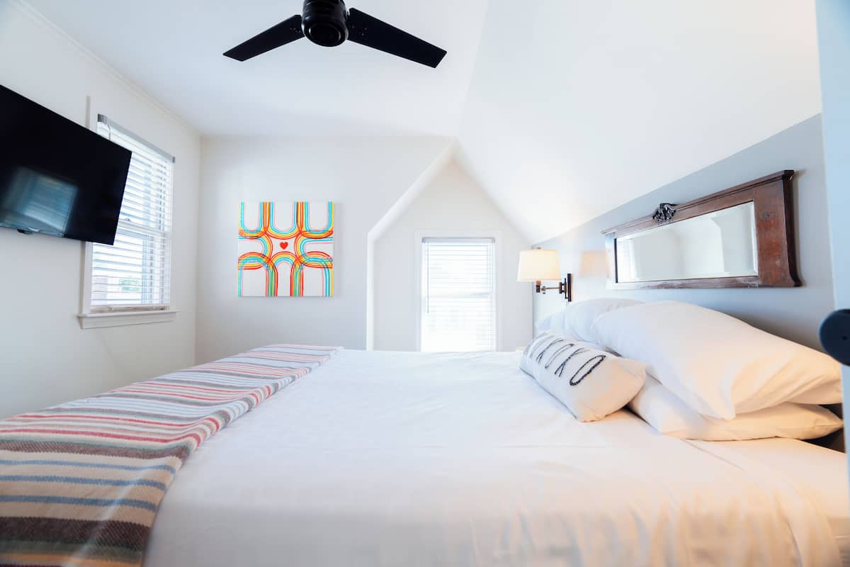 A bedroom with a bed, a ceiling fan, a TV, a window, and a wall art piece.