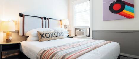 A neatly made bed with a striped blanket, two bedside lamps, and a pillow with the word "XOXO".