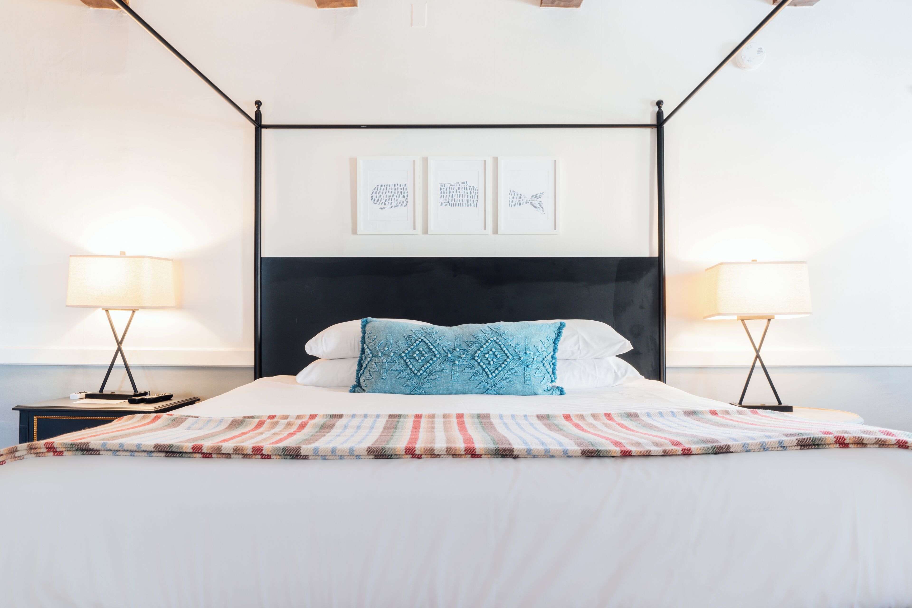 A neatly made bed with a striped blanket, two bedside tables with lamps, and three framed pictures on the wall above the bed.