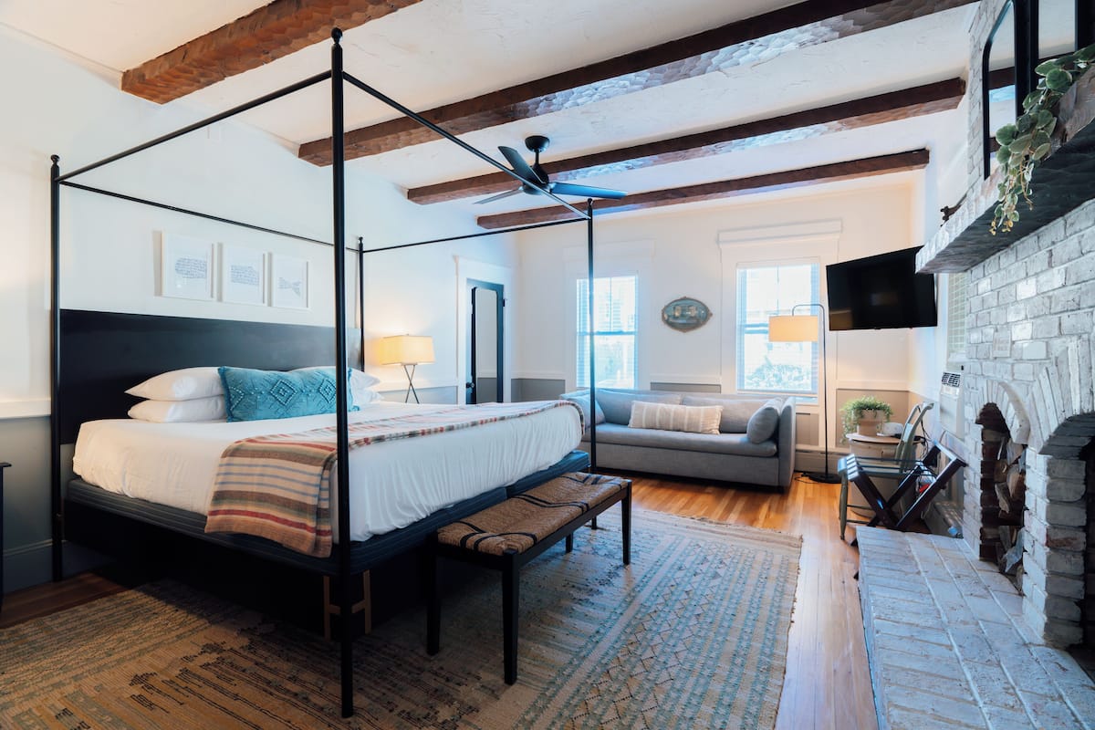 A bedroom with a four-poster bed, a bench, a sofa, a fireplace, and a television.