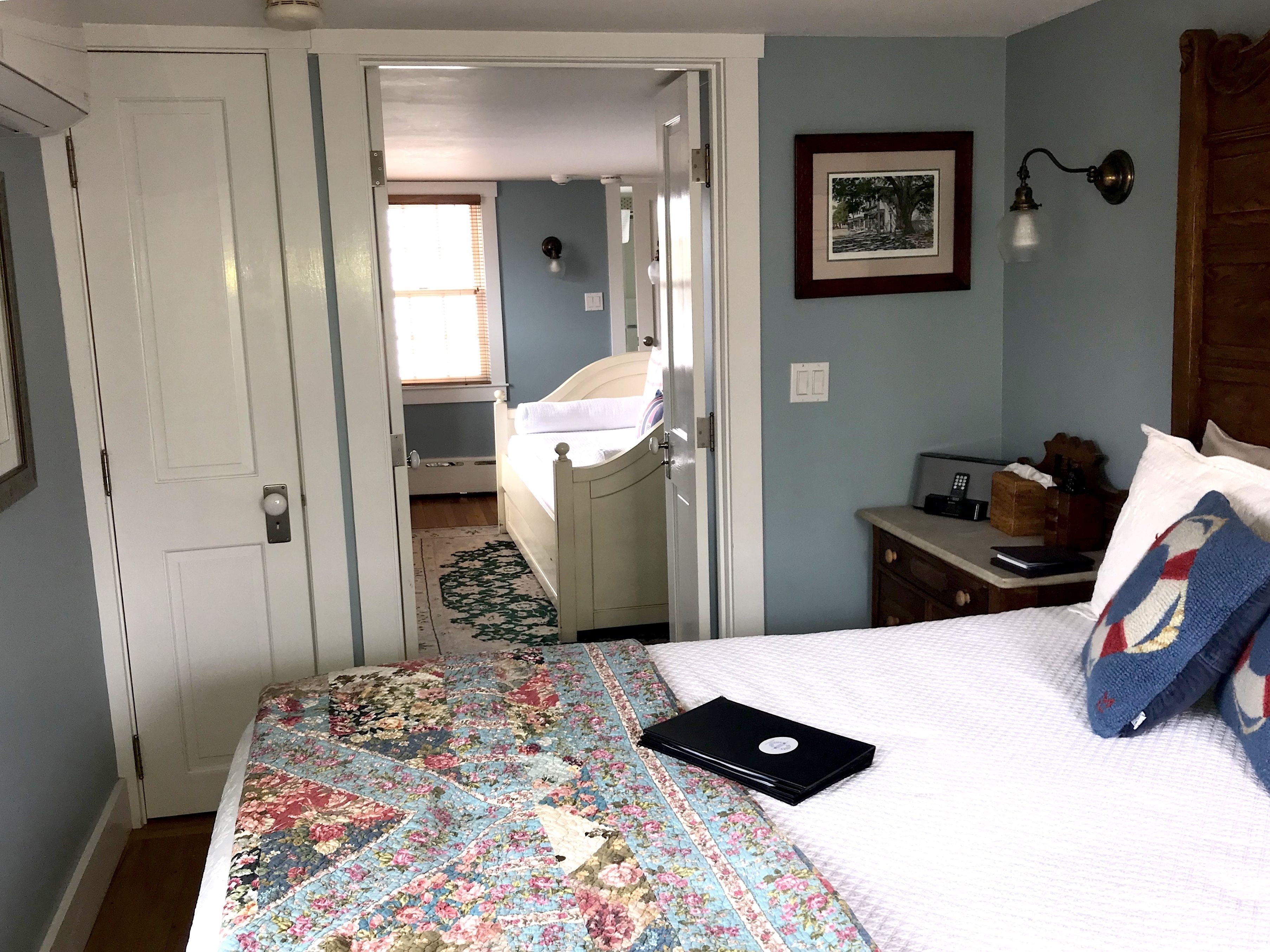 A bedroom with a bed, a desk, a chair, a laptop, and a framed picture on the wall.