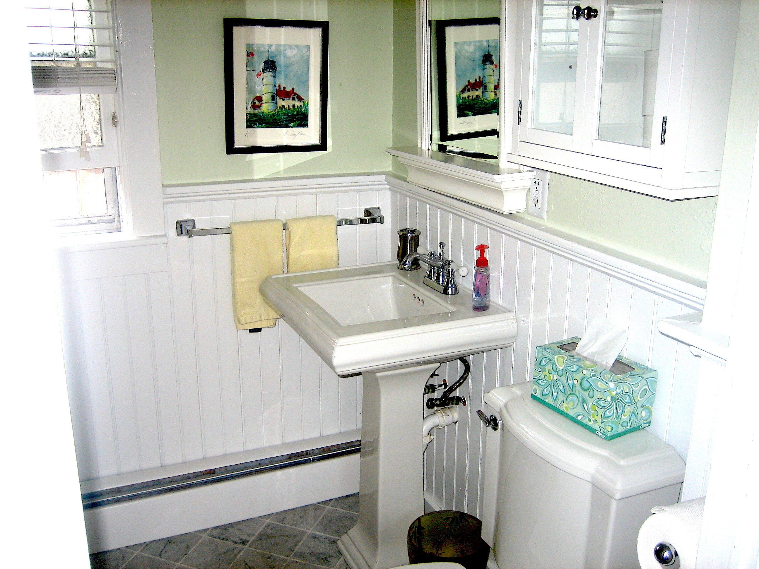A bathroom with a white sink, a toilet, and a mirror. There are towels hanging on the wall and a picture frame above the sink.