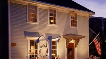 Welcome to REVERIE GUEST HOUSE, a charming two-story guest house with a traditional facade, adorned with a picket fence and beautiful flowering plants.