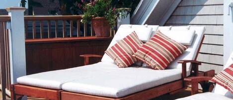 Une terrasse en bois avec deux chaises longues et une plante en pot.