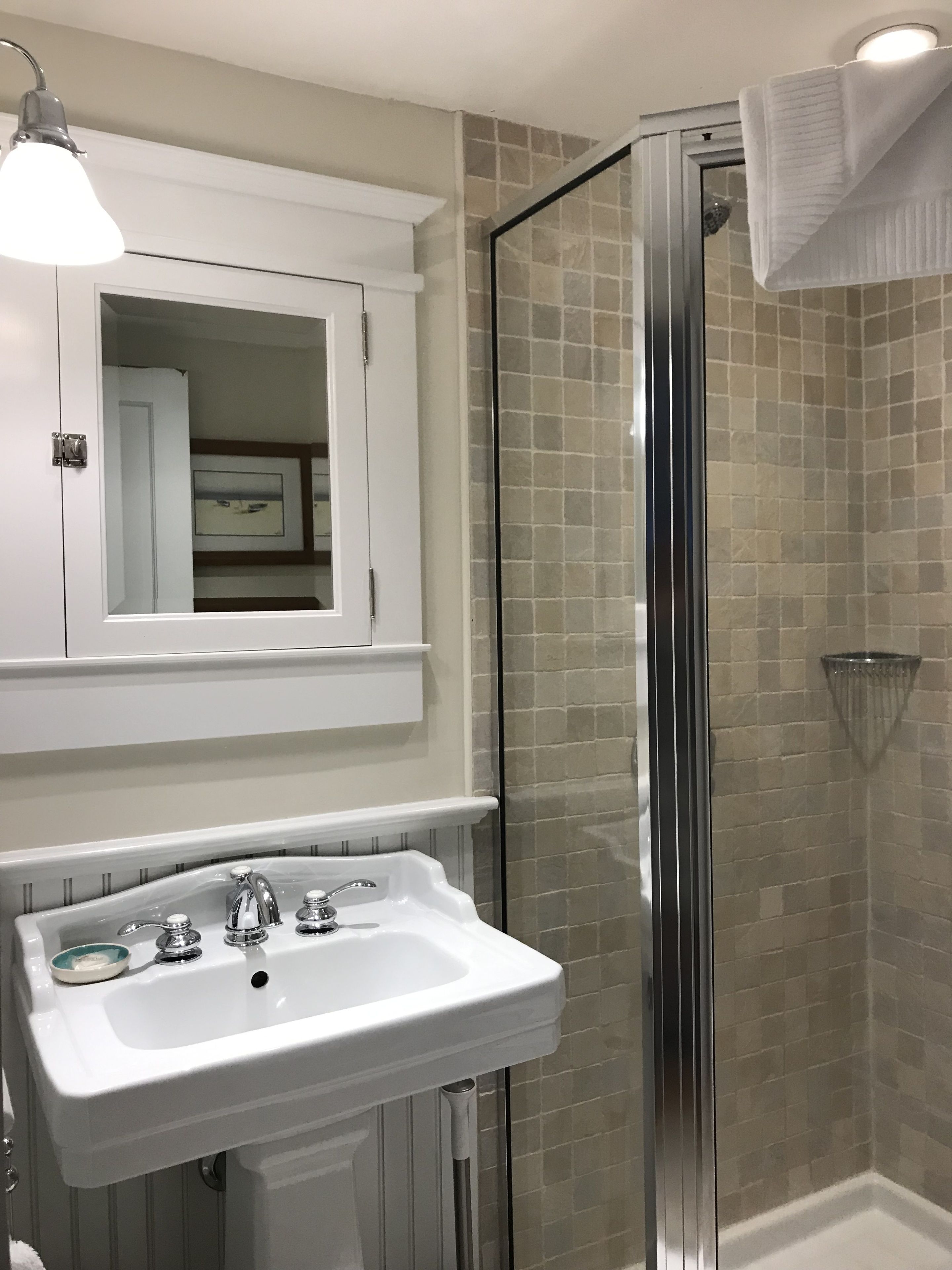 Une salle de bain avec un lavabo blanc, un miroir au-dessus et une cabine de douche en verre.