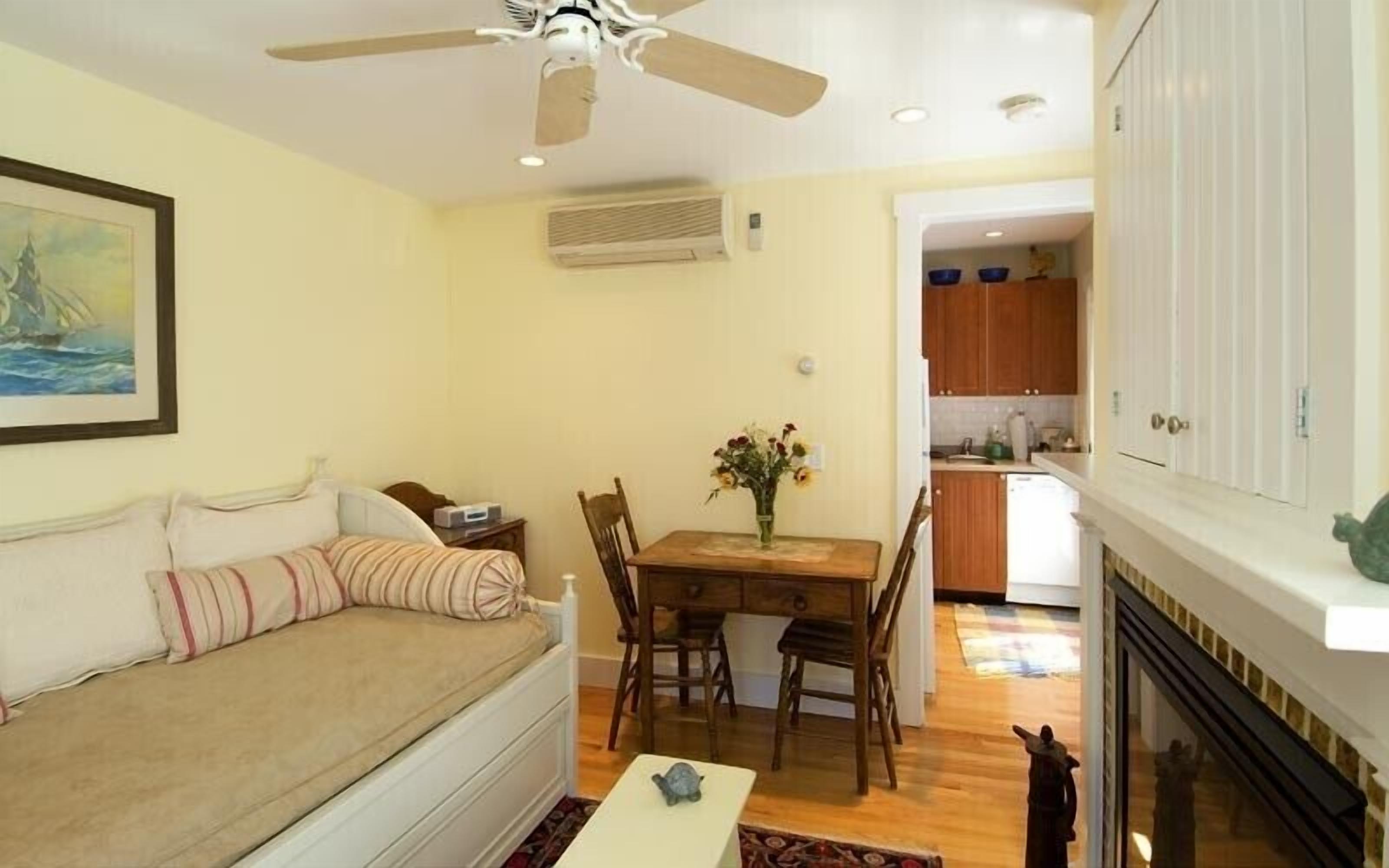 A cozy living room with a sofa, a dining table with chairs, a ceiling fan, and a kitchen in the background.