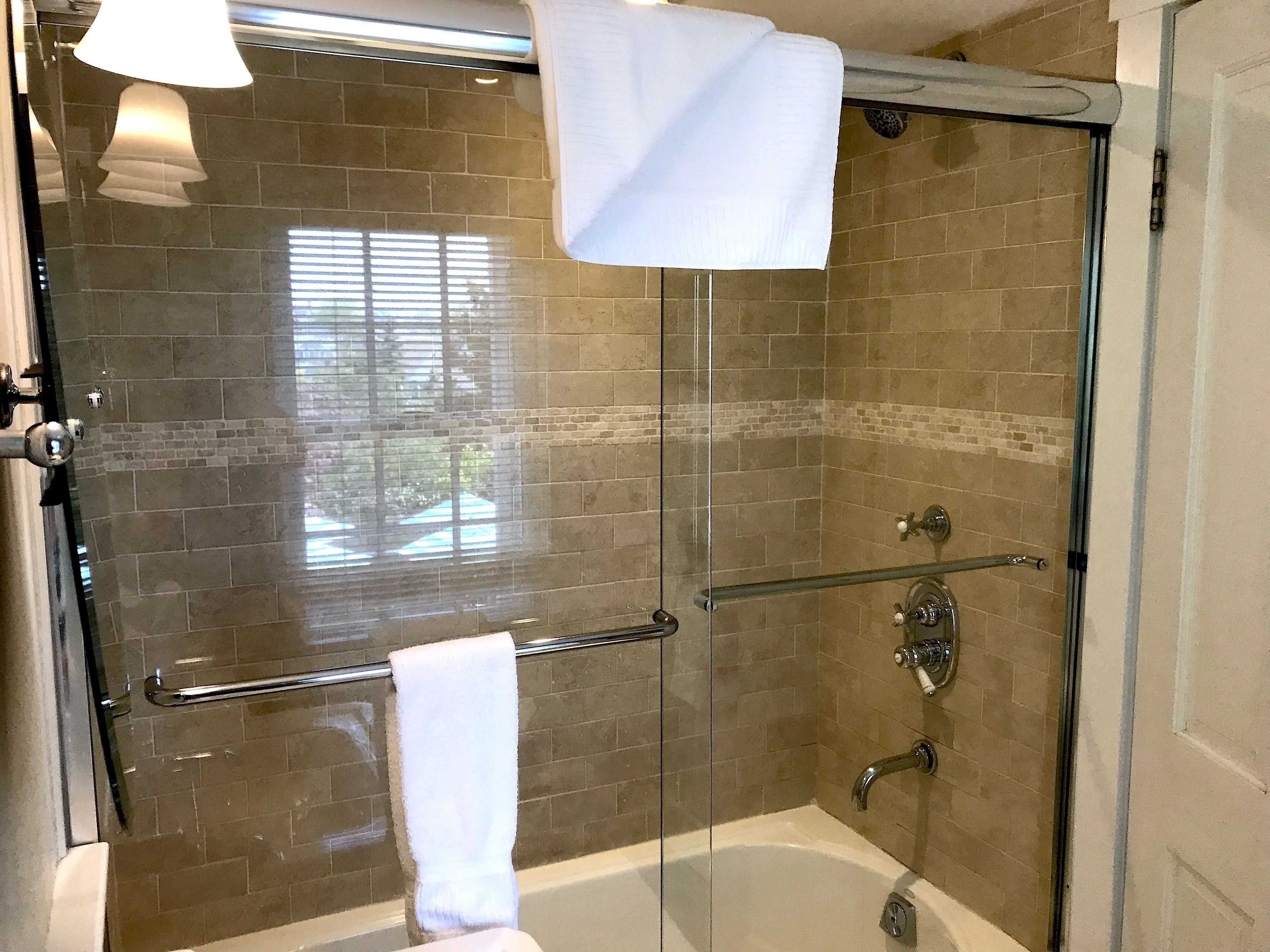 A glass-enclosed shower with a bathtub, a glass door, and a towel rack.