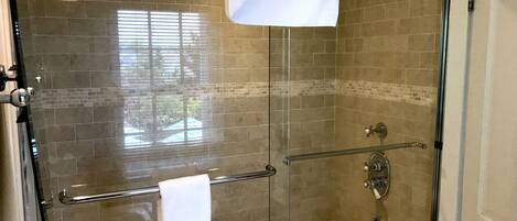 A glass-enclosed shower with a bathtub, a glass door, and a towel rack.