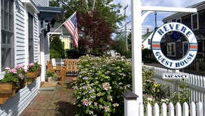 Une maison d’hôtes avec une clôture en bois peinte en blanc, une pancarte indiquant qu’il y a des chambres disponibles et un drapeau américain.