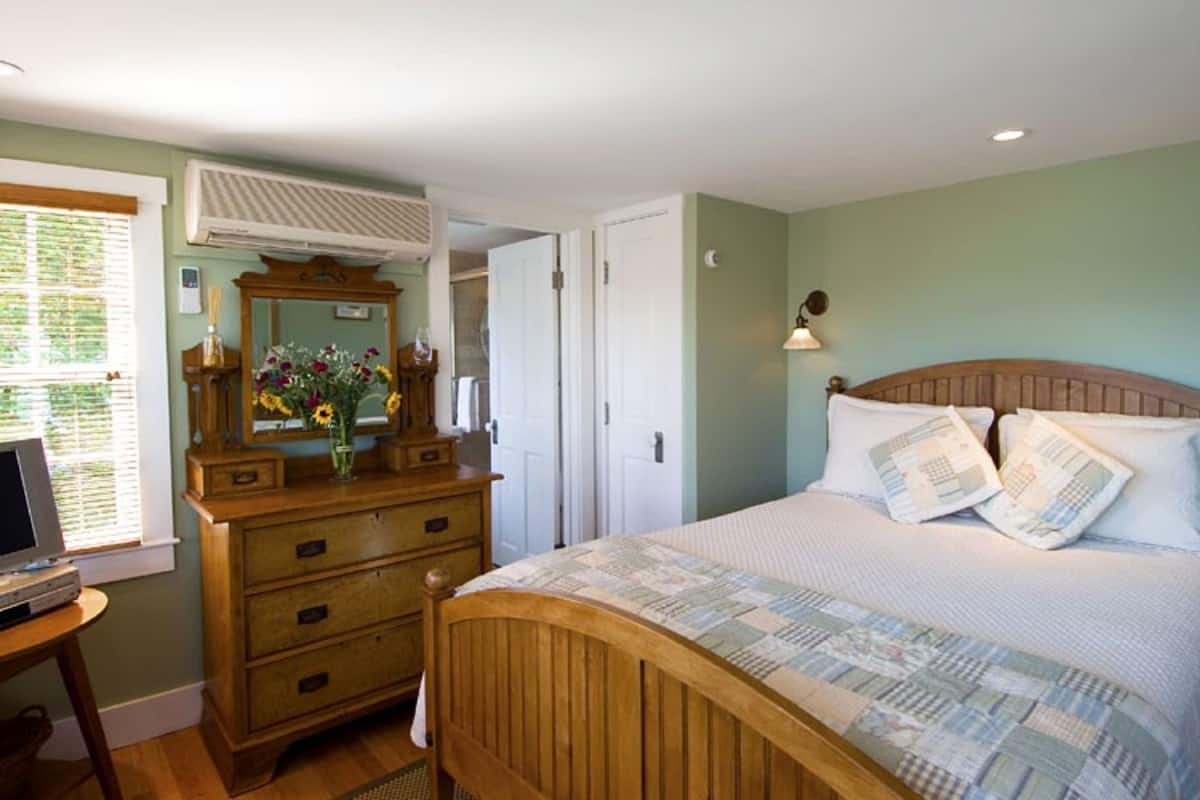 Ein Schlafzimmer mit einem hölzernen Bett, einem Schminktisch, einem Spiegel und einem Fenster mit Jalousien.